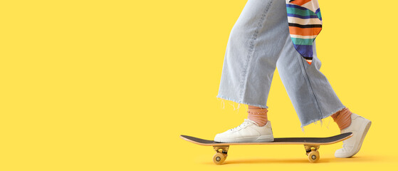 Young woman riding skateboard on yellow background