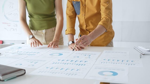 Business professionals analyzing financial reports, pointing at charts during collaborative meeting, discussing data with focused professional demeanor - Powered by Adobe