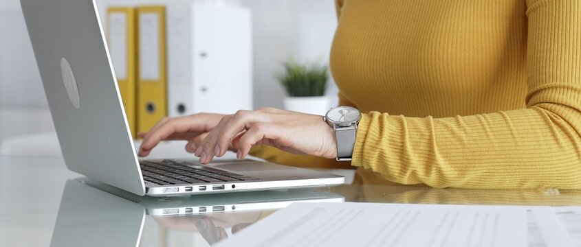 Woman working on laptop, typing on keyboard in office, managing business documents on desk, focusing on digital marketing communication and online data entry