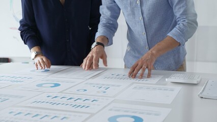 Business professionals analyzing financial charts, gesturing over spreadsheets during collaborative meeting in contemporary workspace, discussing data driven insights