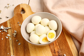 Board with bowl of boiled quail eggs and shells on white wooden background