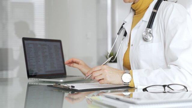 Doctor working on medical records, writing prescription in clinic office, using laptop for patient data management. Medicine, healthcare and science concept