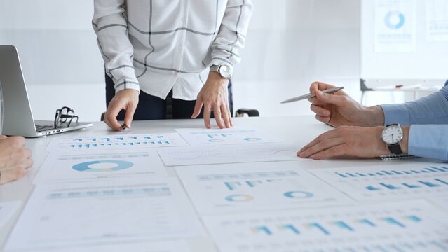 Business team analyzing financial charts and data reports during strategy meeting, hands pointing to documents on table with graphs and diagrams for planning