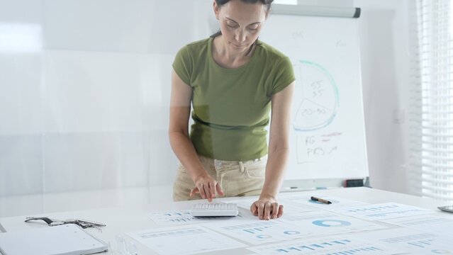 Businesswoman pointing at financial charts and graphs on a table, with a pie chart on a flip chart in the background. Business people concept