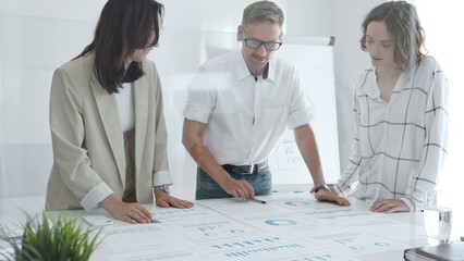 Professional team analyzing financial charts, colleagues reviewing data with focused expressions in modern workplace setting. Business people concept