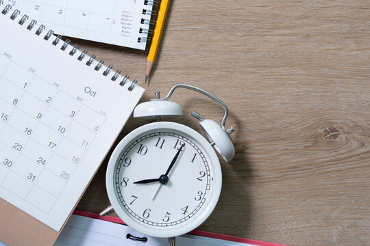 close up of calendar and alarm clock on the wooden table background, planning for business meeting or travel planning concept