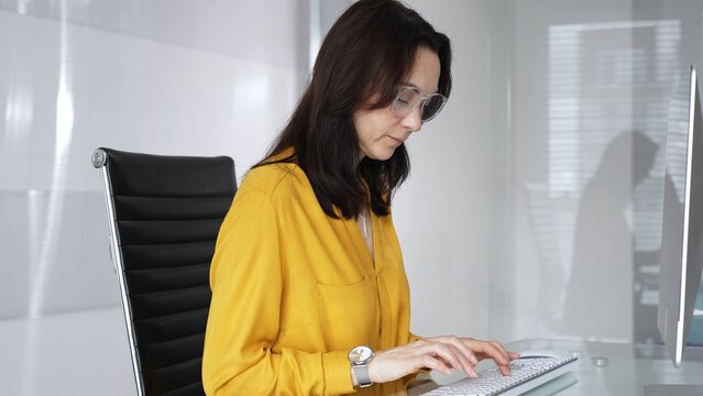 Professional businesswoman wearing yellow casual blouse is analyzing data and information, typing on computer keyboard in modern office, concentrating on work online. Audit in business
