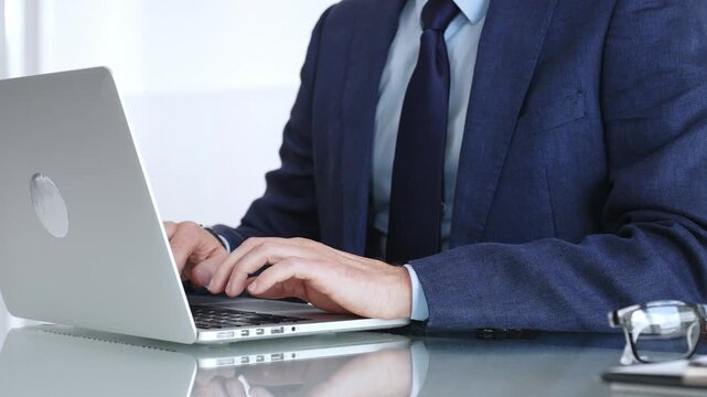 Professional businessman working on laptop computer, typing on keyboard in modern office, managing business tasks. Business people concept