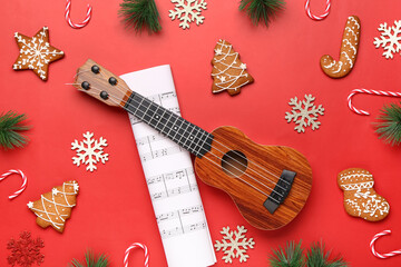 Composition with ukulele, music sheet, Christmas decorations and cookies on red background