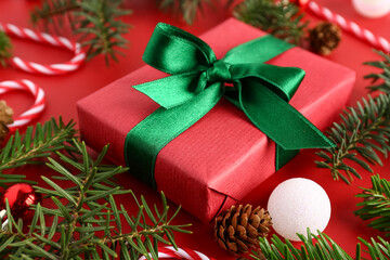 Christmas gift box with balls, fir tree branches and candy cane toys on red background