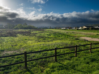 Tranquil Open Field With Wooden Fence, Suburban Homes, and Dramatic Stormy Sky at Sunset