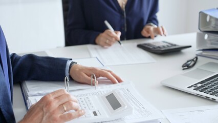 Close up of male accountant hands using calculator and collaborating with female colleague in a modern office, calculating taxes and analyzing financial data. Audit and taxes in business