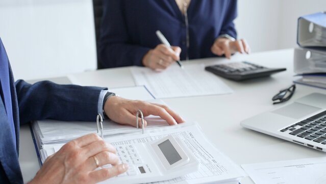 Close up of male accountant hands using calculator and collaborating with female colleague in a modern office, calculating taxes and analyzing financial data. Audit and taxes in business