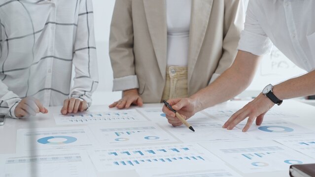 Business team working on financial charts and graphs, pointing at statistics and discussing business project data in modern office. Business people concept