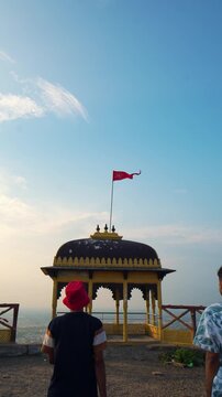 Three hikers trekking during sunset in the mountains under a partly cloudy sky, with a temple creating a breathtaking backdrop at Samai Mata Mandir, Banswara, near Udaipur, Rajasthan, India.