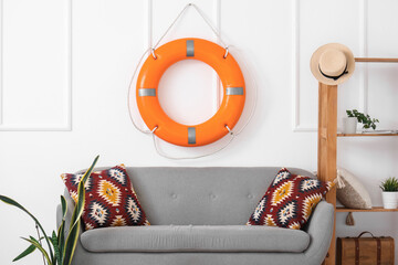 Cozy sofa with cushions, shelving unit, houseplant and lifebuoy ring in living room
