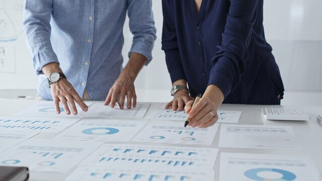 Professional team reviewing financial documents, pointing at charts on desk, collaborating to analyze data and strategize business growth. Business people concept