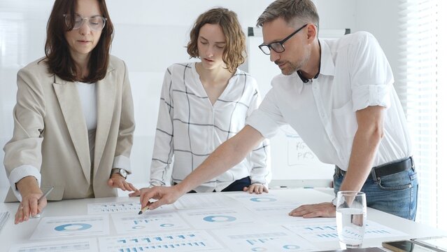 Professional team analyzing financial data, corporate colleagues carefully examining charts and graphs in modern workplace. Business people concept - Powered by Adobe