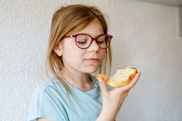 Little school girl eating bread with butter for breakfast. Happy cute child with eyeglasses having healthy snack.