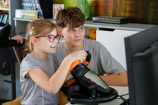 Happy little girl and teenage boy playing racing video game with steering wheel controller. Siblings enjoying computer game together at home. Real life moment of fun and bonding. - Powered by Adobe