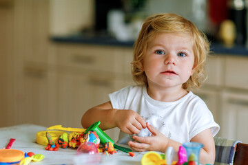 Adorable cute little toddler girl with colorful clay at home. Healthy baby playing and creating toys from play dough at nursery or playschool. Small kid molding modeling clay, creative activity
