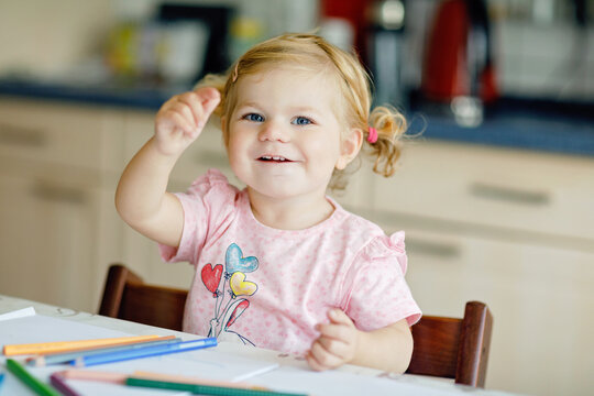 Cute adorable baby girl learning painting with pencils. Little toddler child drawing at home, using colorful felt tip pens. Healthy happy daughter experimenting with colors at home or nursery.
