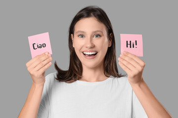 Smiling young woman holding pink sticky notes with "ciao" and "hi" greetings, communication and language learning, happy © Pixel-Shot