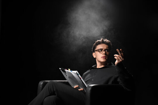 Male screenwriter with scenario in armchair on dark background