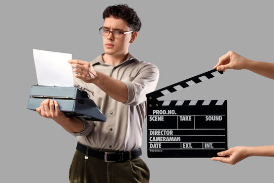 Male screenwriter using typewriter and female hands with movie clapper on grey background