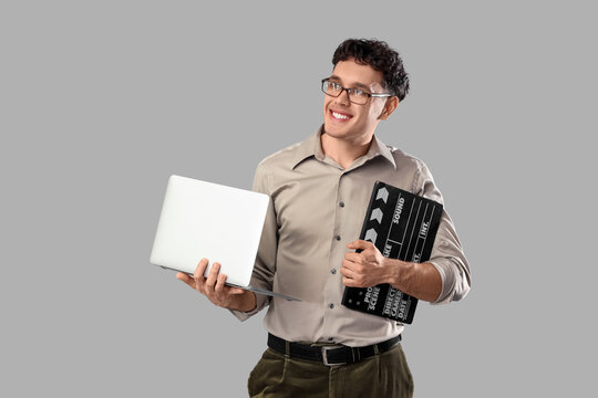 Male screenwriter with laptop and movie clapper on grey background