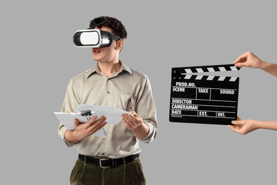 Male screenwriter in VR glasses holding scenario and female hands with movie clapper on grey background