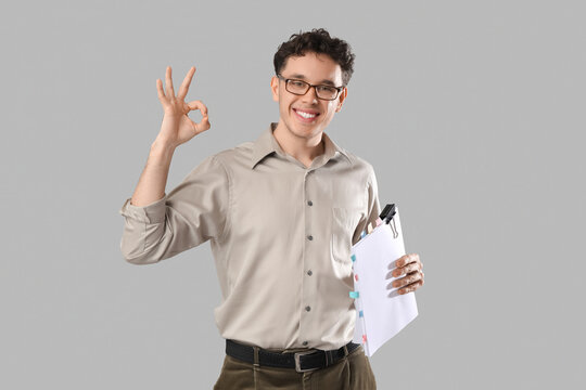 Young man with scenario showing OK on grey background