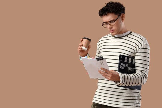 Male screenwriter with coffee and movie clapper reading scenario on beige background