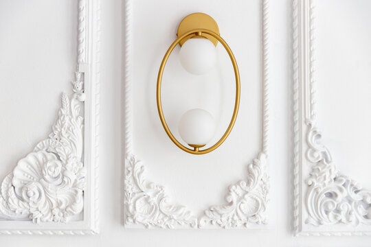 Elegant oval-shaped brass and white glass sconce (wall light) mounted on a classic white wall with detailed plaster molding and decorative trim