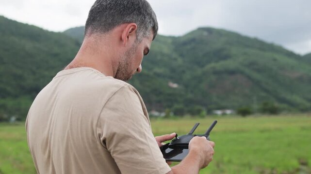 A man operates a drone against a backdrop of green hills.