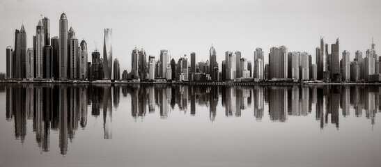 Monochrome city skyline with tall skyscrapers reflecting on calm water under a cloudy sky, Dubai Marina bay UAE
