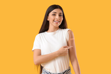 Obraz premium Young woman pointing at medical patch after vaccination on yellow background. Immunity concept