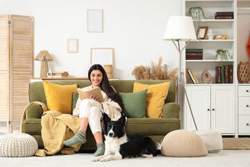 Young woman reading book on sofa with Border Collie dog at home