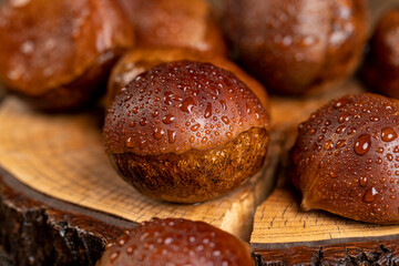 a hard edible chestnut fruit in a brown shell covered with water droplets on a wooden table, a group of wet and fresh chestnut with a brown hard shell