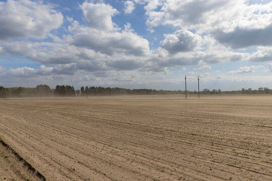 dust storm in windy weather in the field after plowing and preparing the field for sowing, flying dust from strong winds in the field in the spring season, blue sky with clouds