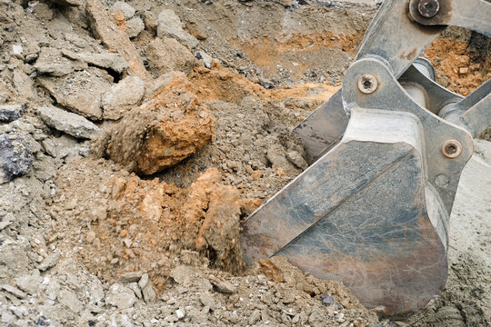 Construction workers are repairing a road by excavating and drilling the pavement to fill underground voids with specially mixed concrete. Heavy machinery and roadwork safety cones are visible.