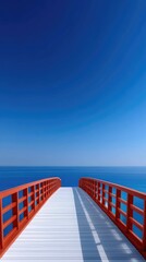 Wooden Boardwalk With Red Railings Leads To The Vast Deep Blue Ocean Under A Clear Bright Sky