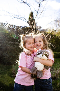 Young twin sisters hugging each other while holding raccoon stuffed toy