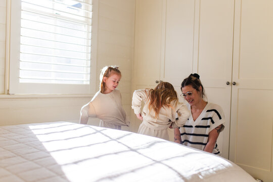 Young girls standing beside the bed getting dressed while mum kneels on the floor