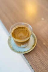 Layered dirty coffee in a glass espresso shot poured over cold milk on wooden table