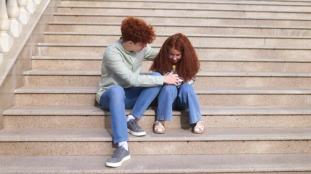Redhead preteen boy comforting upset girl sitting together on outdoor steps