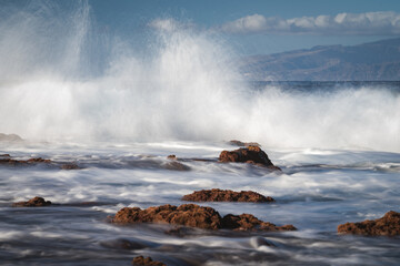 Powerful ocean waves crashing against volcanic rocks on the coast. Long-exposure seascape with dramatic motion blur and splashing water, Tenerife coastline, Spain.