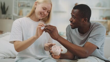 Save money and form family budget, woman and man putting coins into piggy bank. Portrait of happy interracial loving couple, financial literacy and savings for realize dreams, multiethnic couple - Powered by Adobe