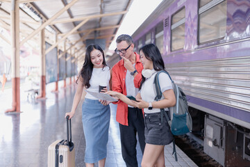Group of diverse friends standing on a train station platform, holding a paper map and smartphone, discussing their travel plans and destination before boarding
