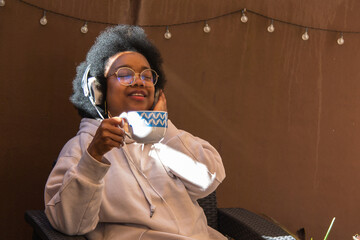 African American woman relaxing on the terrace of her house listening to music with headphones